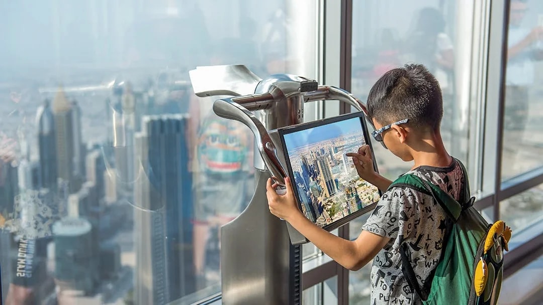 Child using electronic telescope at Level 124, Burj Khalifa, viewing Dubai skyline.