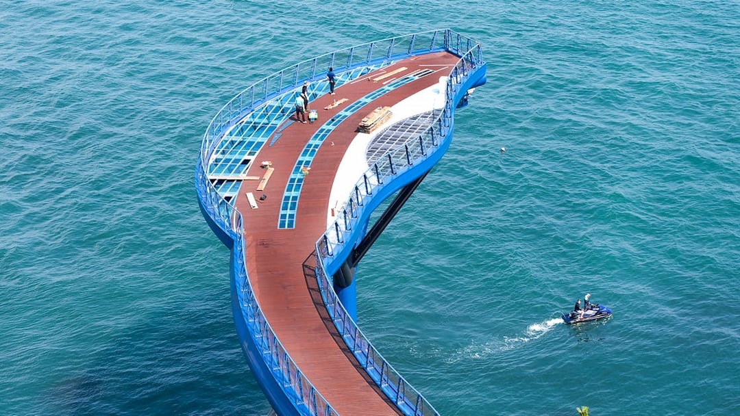 Blueline Park Sky Capsule platform over ocean in Busan, South Korea, with people and jet ski nearby.