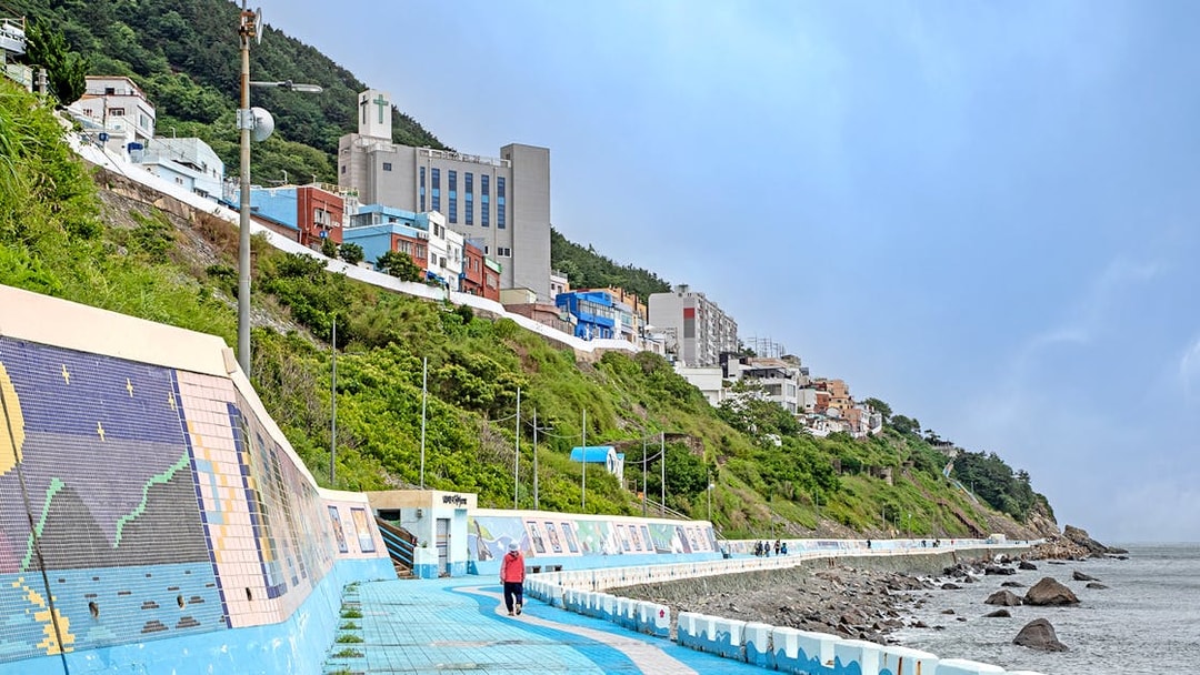 Seaside walkway with colorful murals and hillside buildings in Busan, part of the Blueline Park Sky Capsule Tour.