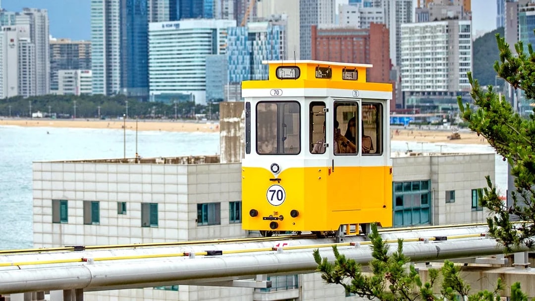 Yellow sky capsule on track with Busan cityscape in background.