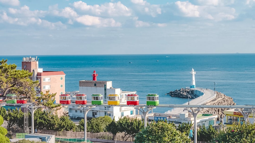 Blueline Park Sky Capsule overlooking Busan coastline with lighthouse and colorful buildings.