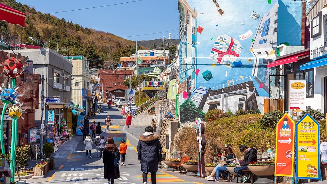 Street view of Gamcheon Culture Village in Busan with colorful murals and tourists exploring.