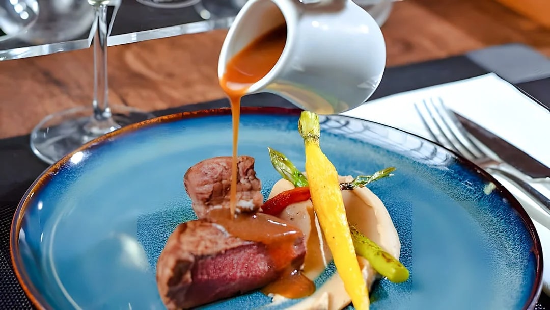 Waiter pouring sauce over steak dish inside Bustronome Paris.