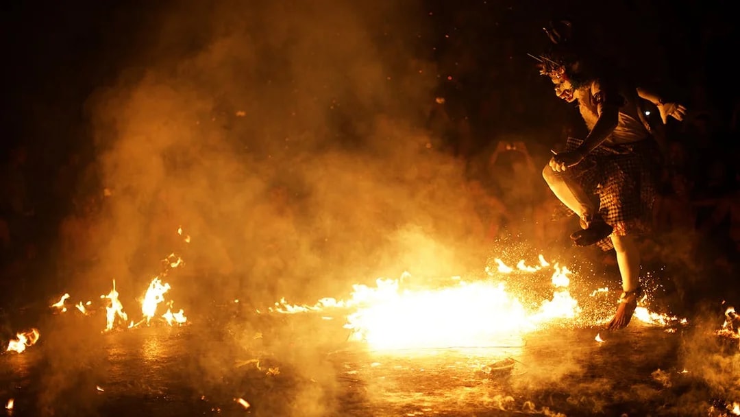 Traditional fire dance performance in Bali, Indonesia, with performer leaping through flames.