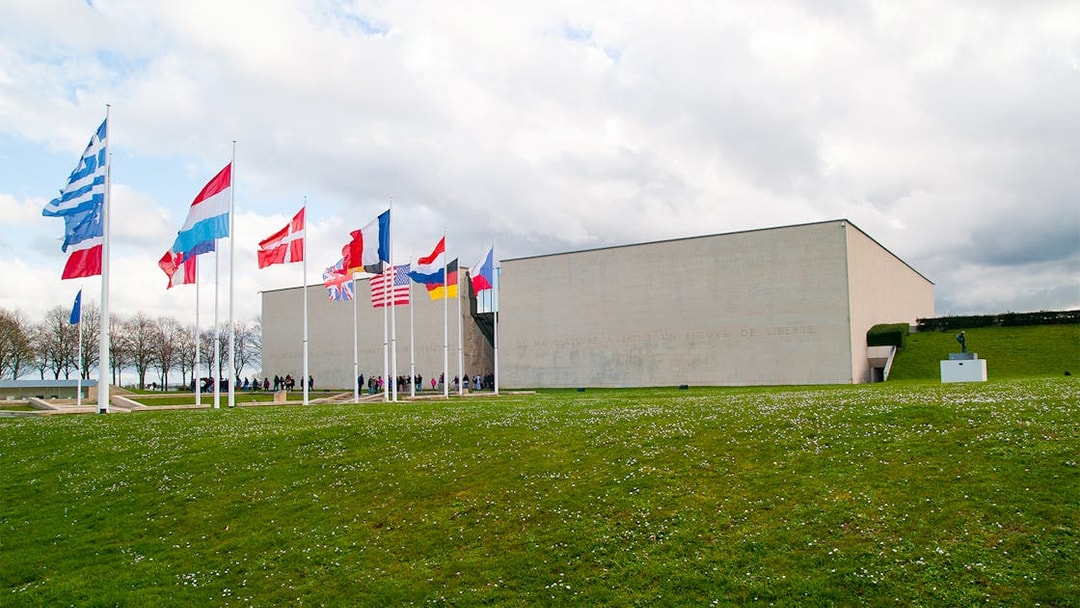 Flags outside the Caen Memorial Museum in France, with visitors entering.