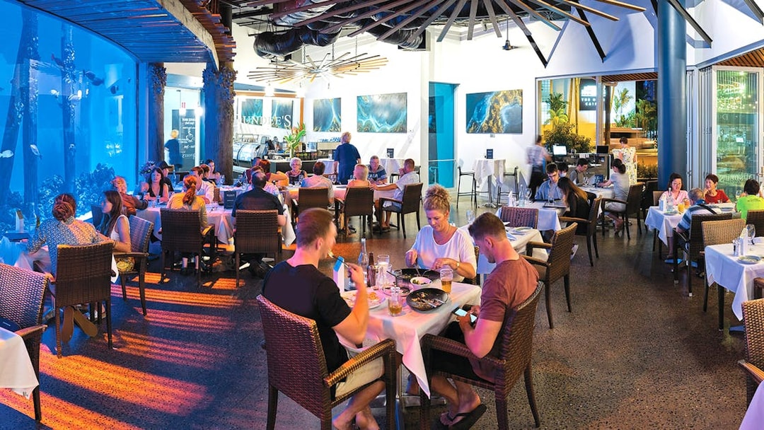 Dining area at Cairns Aquarium by Twilight with guests enjoying meals near large aquarium display.