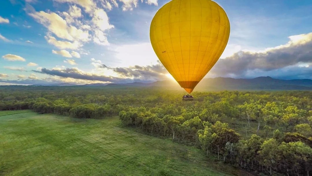 Hot air balloon over lush landscape at sunrise in Cairns, Australia.