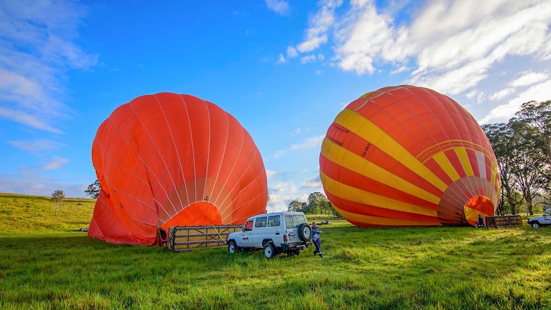 Hot air balloons inflating on a grassy field in Cairns, Australia, with a vehicle nearby.