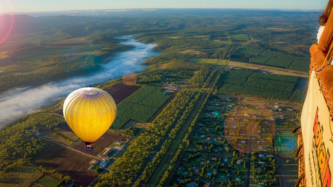 Hot air balloon floating over lush landscape with distant mountains and morning mist.