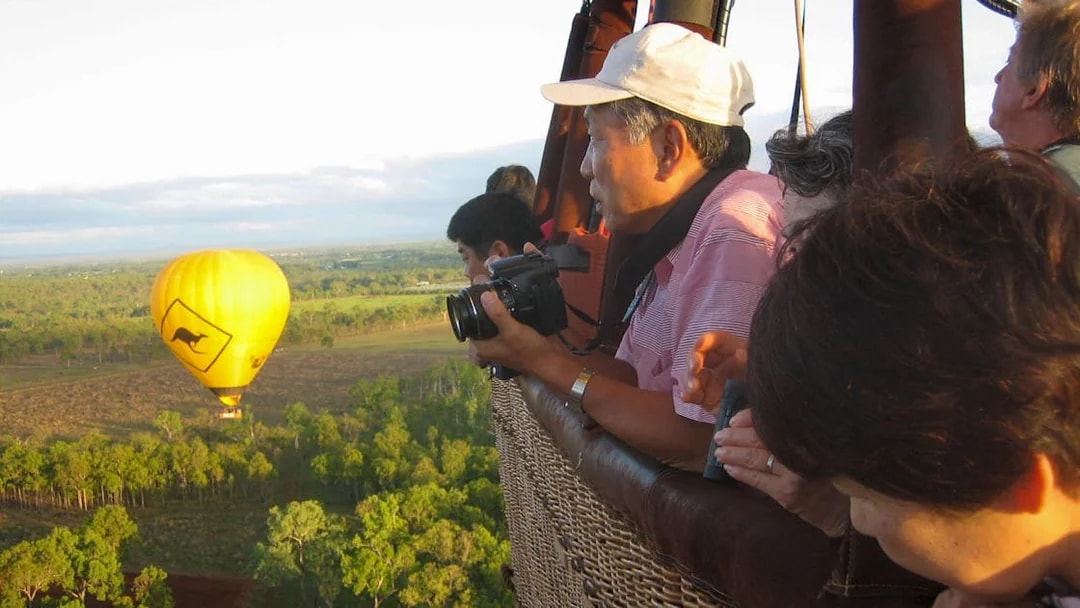 Hot air balloon over Cairns landscape with passengers enjoying the view.
