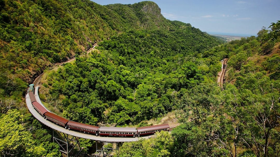 Aerial view of Kuranda Scenic Railway winding through lush green rainforest.