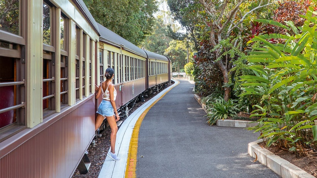 Tourist stepping off Kuranda Scenic Rail surrounded by lush greenery.