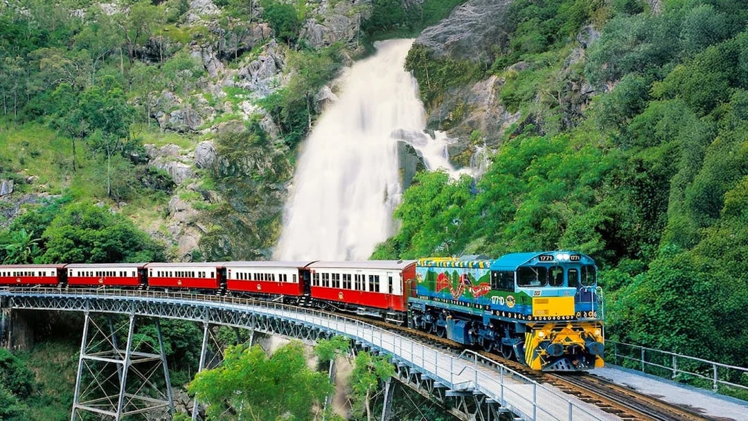 Kuranda Scenic Railway train crossing bridge with waterfall in background, Queensland, Australia.