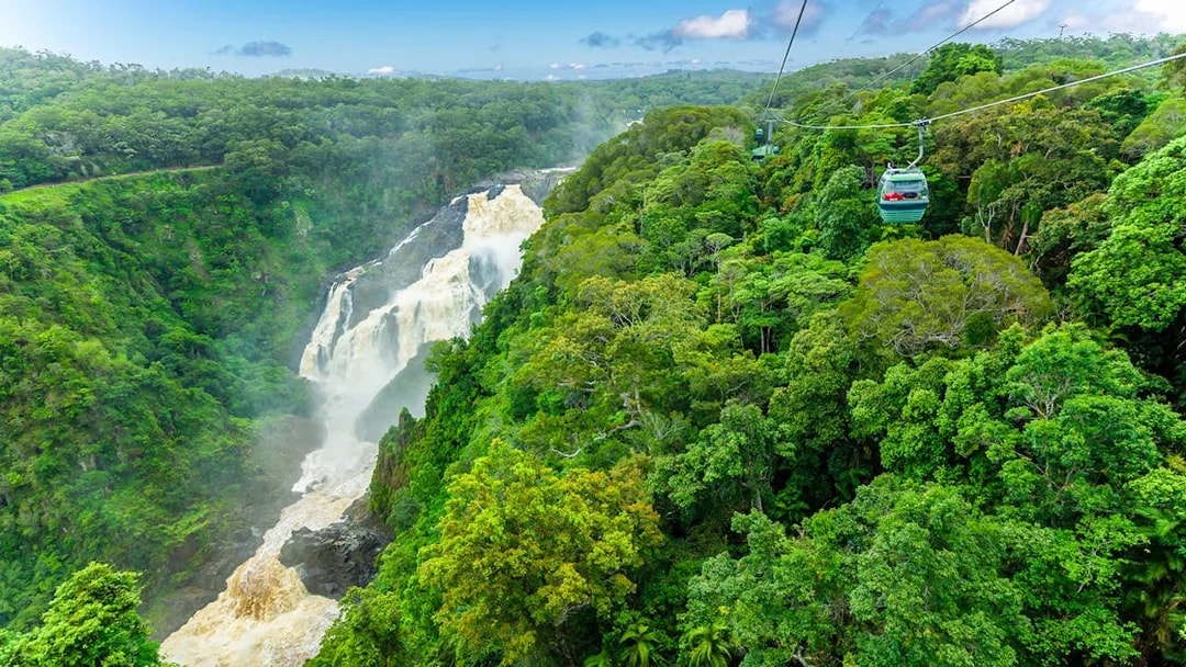 Skyrail cable car gliding over Kuranda Rainforest with waterfall view.