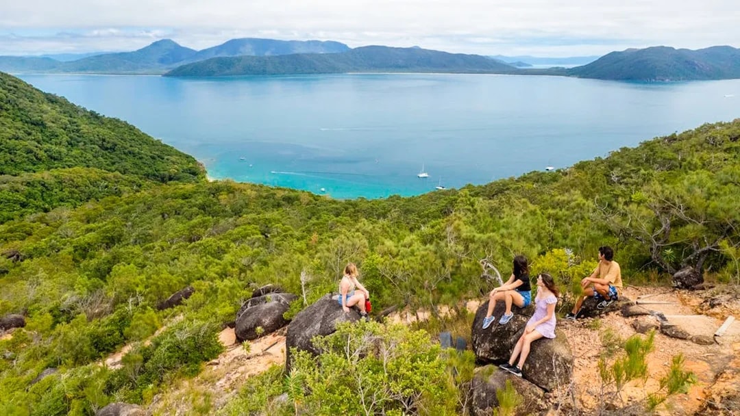 Tourists sitting on rocks overlooking ocean and forest on Fitzroy Island trail.