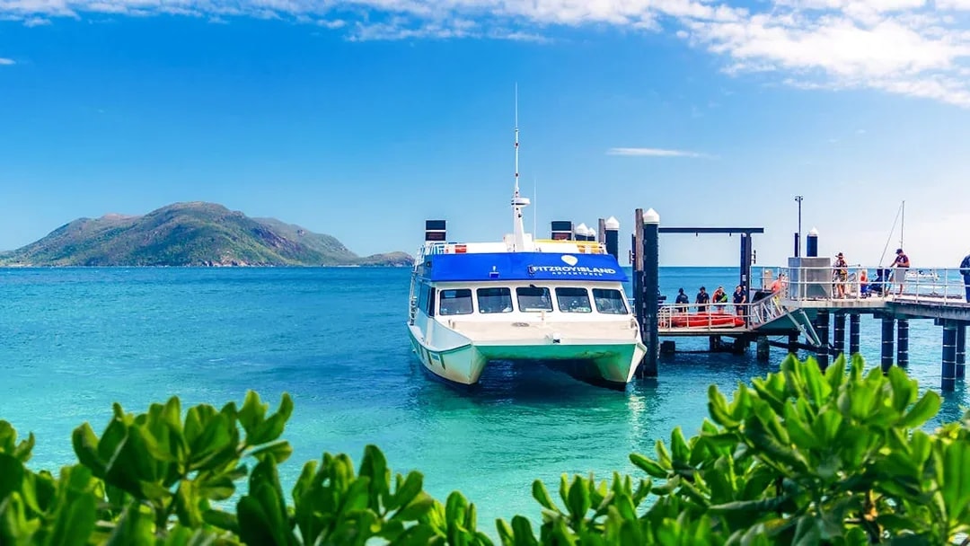 Ferry docked at Fitzroy Island pier with lush greenery and ocean view, Cairns half-day cruise.