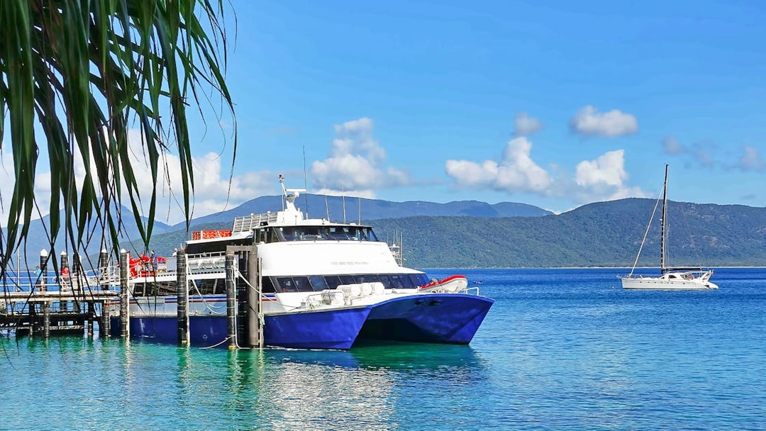 Tourists boarding a boat at Fitzroy Island pier, with lush hills and clear waters, Australia.