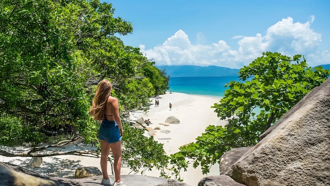 Tourists walking along a sandy beach on Fitzroy Island, surrounded by lush greenery and ocean views.