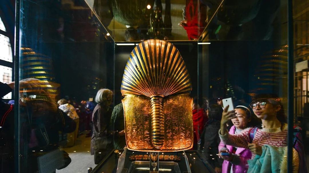 Golden Egyptian artifact displayed in museum exhibit with visitors observing.