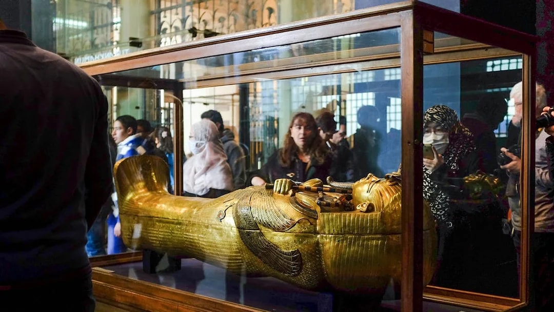Golden sarcophagus displayed in a museum exhibit with visitors observing.