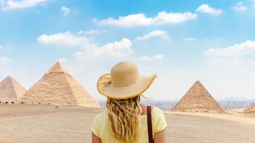 Tourist facing Giza Pyramids in Egypt under a clear sky.