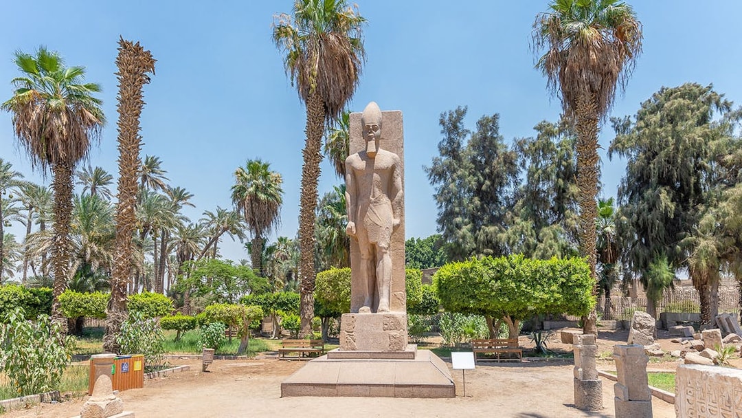 Statue of Ramses II surrounded by palm trees in Memphis, Egypt.