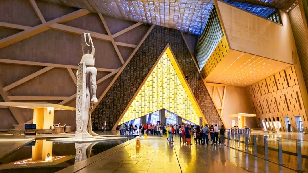 Visitors exploring the Grand Egyptian Museum interior with large statue and modern architecture.