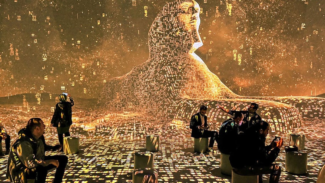 Visitors seated around digital Sphinx projection with hieroglyphs.