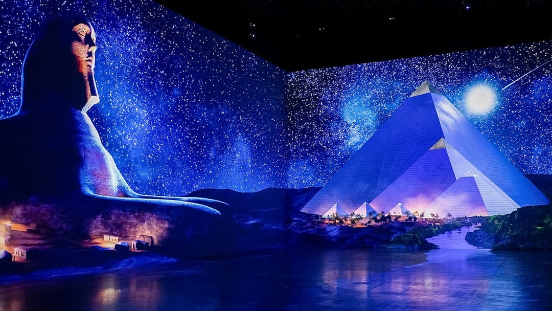 Digital projection of the Sphinx and pyramids beneath a starry night sky.