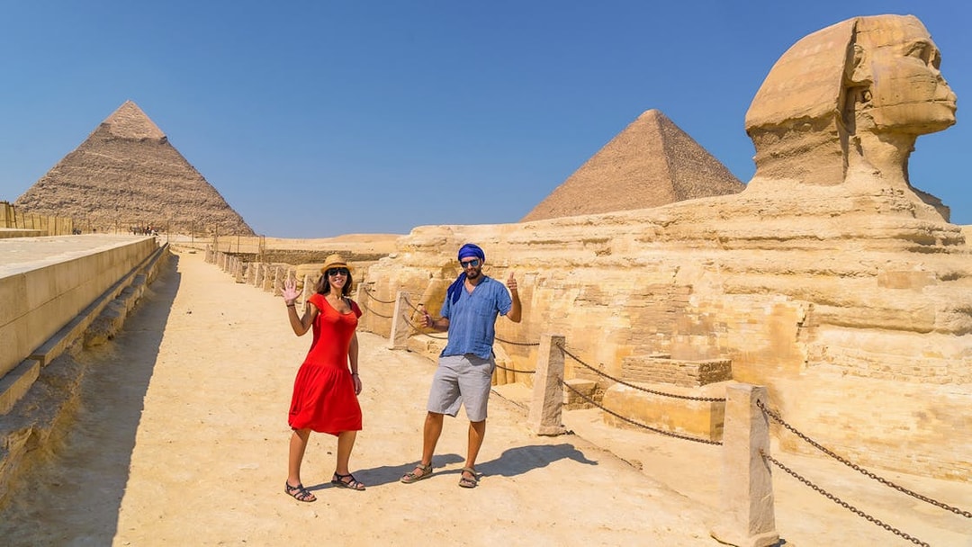 Tourist couple posing at The Great Sphinx of Giza with pyramids in the background.