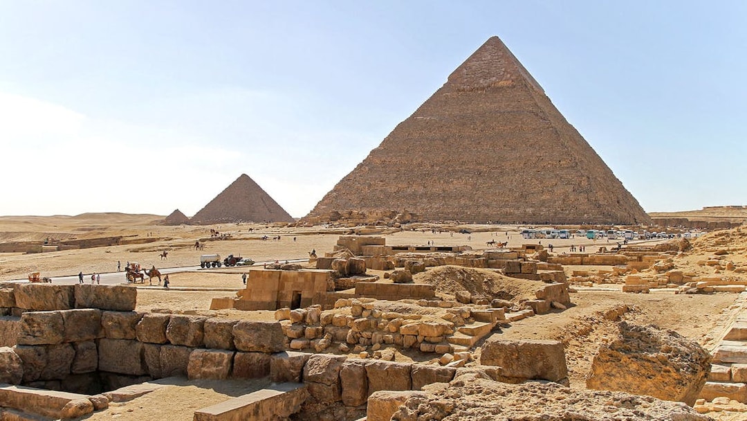 Pyramids of Giza on the Giza Plateau with tourists and camels in the foreground.