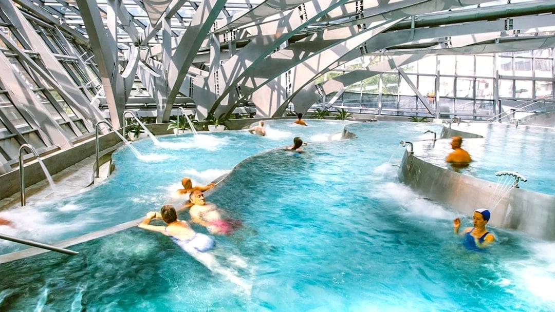 Visitors enjoying thermal pools at Caldea spa in Andorra with modern architecture.