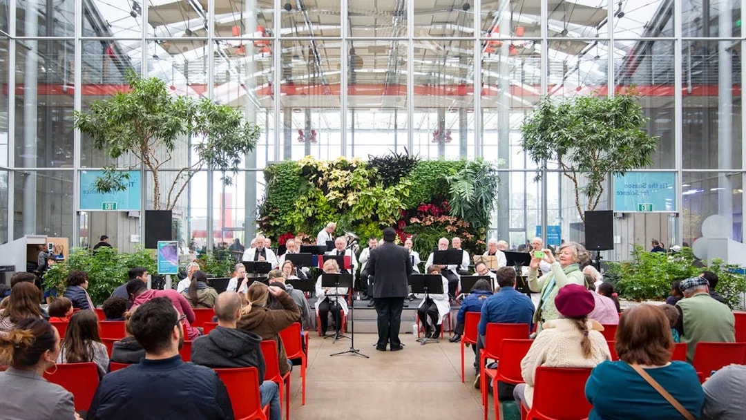 Orchestra performing at California Academy of Sciences with audience seated in red chairs.