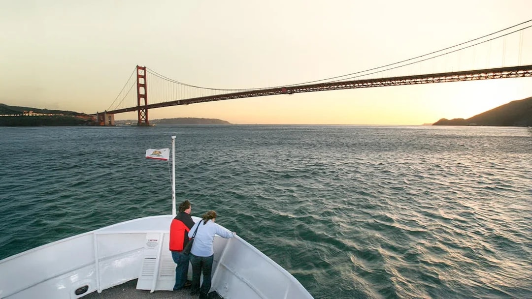 Guests on deck viewing Golden Gate Bridge during California sunset cruise.