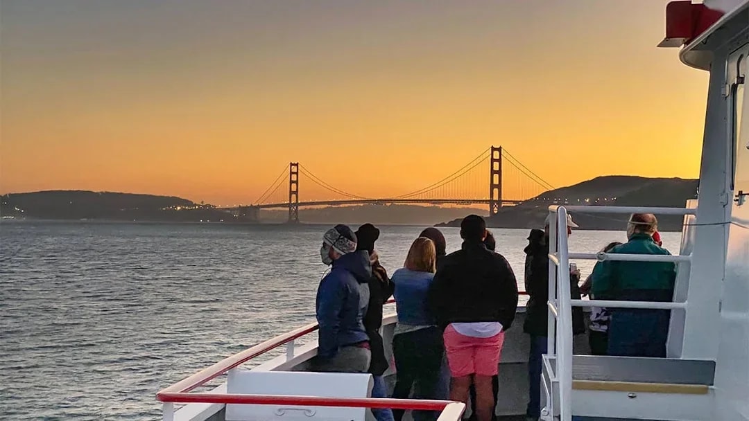Guests on deck viewing Golden Gate Bridge during California sunset cruise.