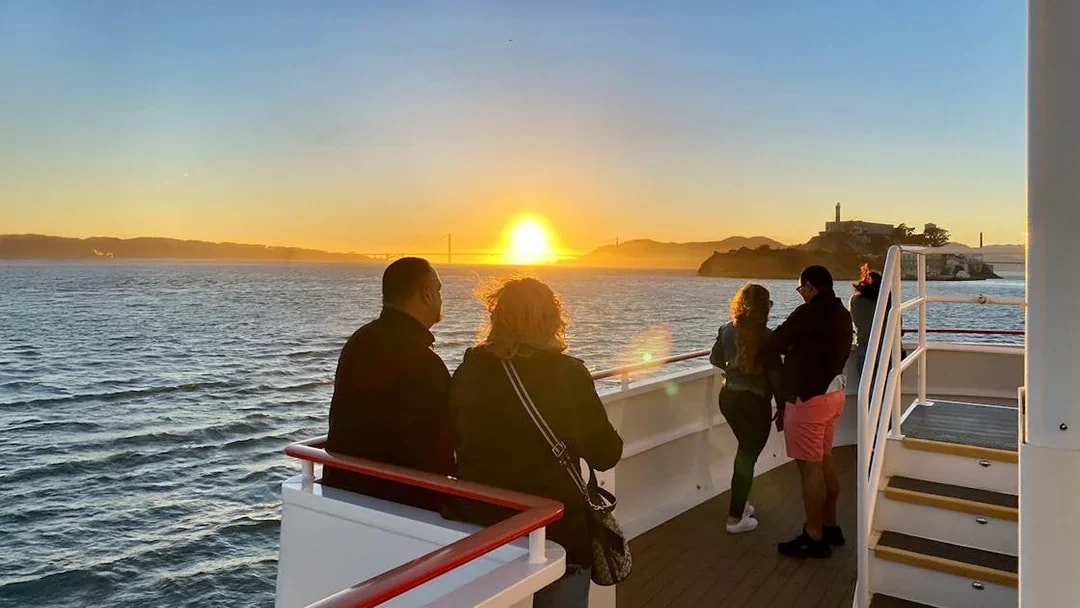 Guests on deck watching sunset during California cruise with Golden Gate Bridge in view.