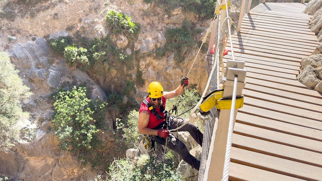 Person rappelling beside a wooden walkway on Caminito del Rey, Spain.