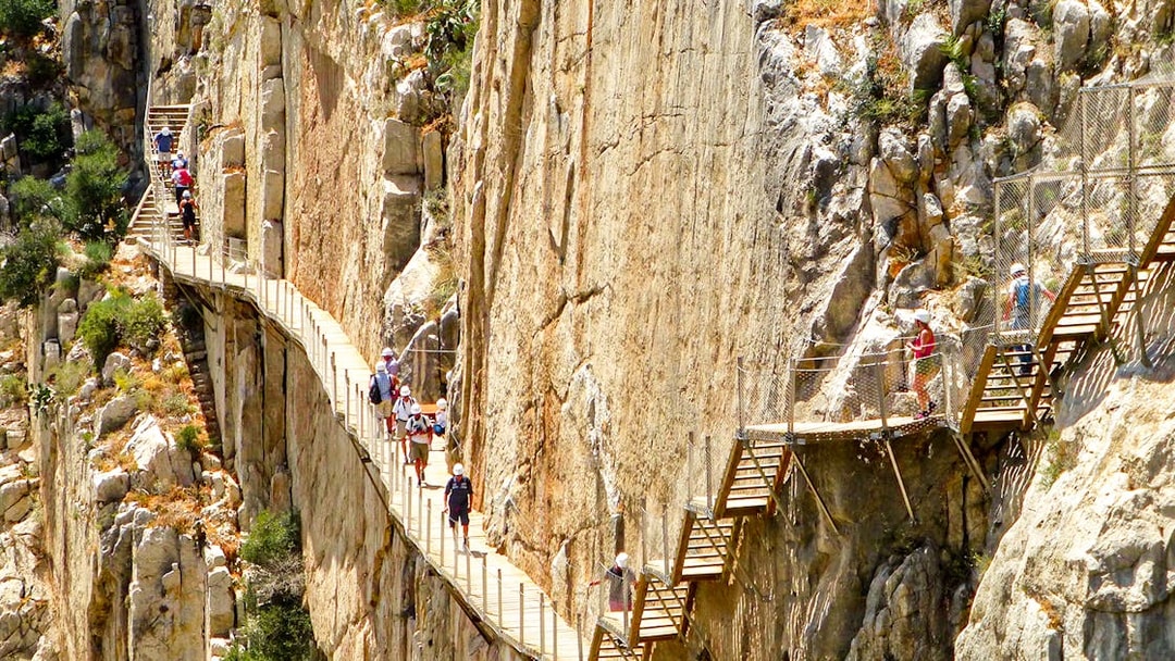 Hikers on Caminito del Rey walkway along steep cliffs in Malaga, Spain.