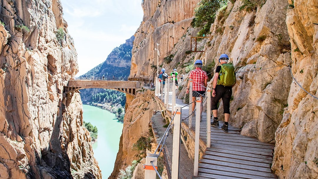 Hikers on Caminito del Rey trail in Málaga, Spain, walking along a cliffside path.