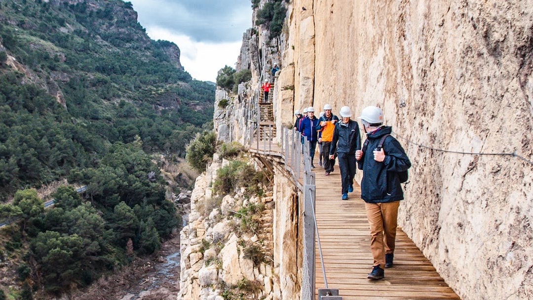Trekkers walking along a narrow path on a guided tour of Caminito del Rey, Spain.