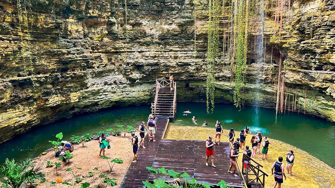 Tourists swimming and relaxing at a cenote with lush greenery and rock formations.