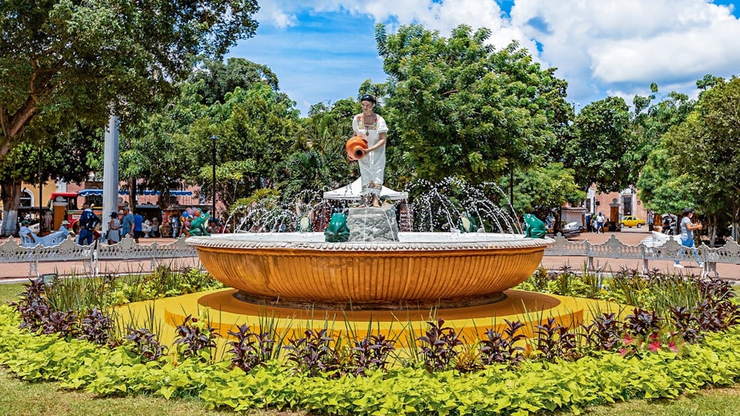 Fountain with statue in Valladolid's central park, Mexico, surrounded by greenery.