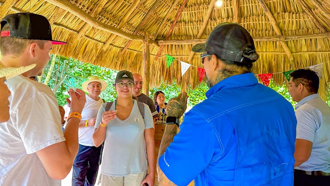 Tourists tasting tequila under a thatched roof during Chichen Itza tour.