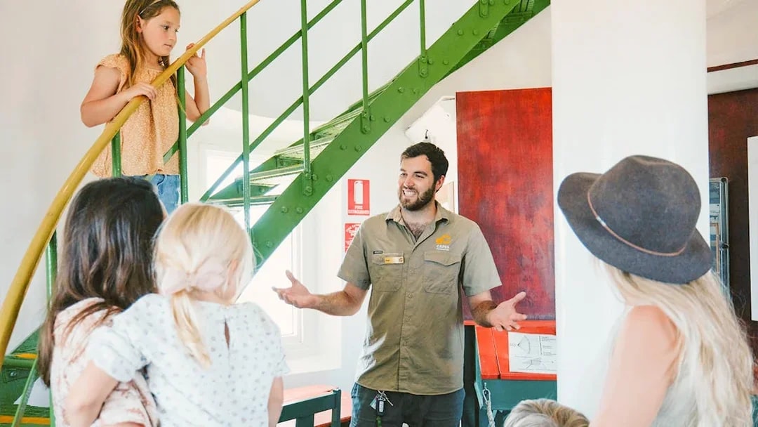 Tour guide explains to family inside Cape Naturaliste Lighthouse near spiral staircase.