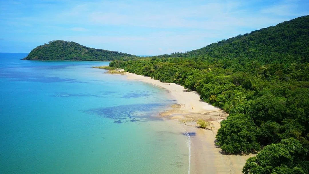 Cape Tribulation beach with lush rainforest and clear blue water, Australia.
