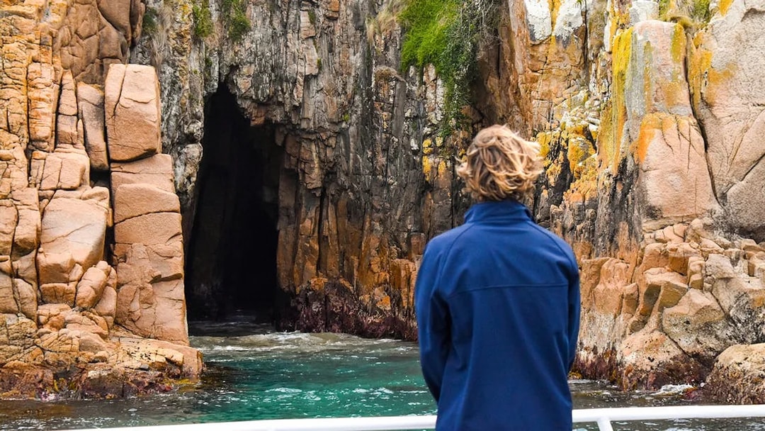 Person viewing rocky cliffs and cave from a boat on Cape Woolamai cruise, Phillip Island.