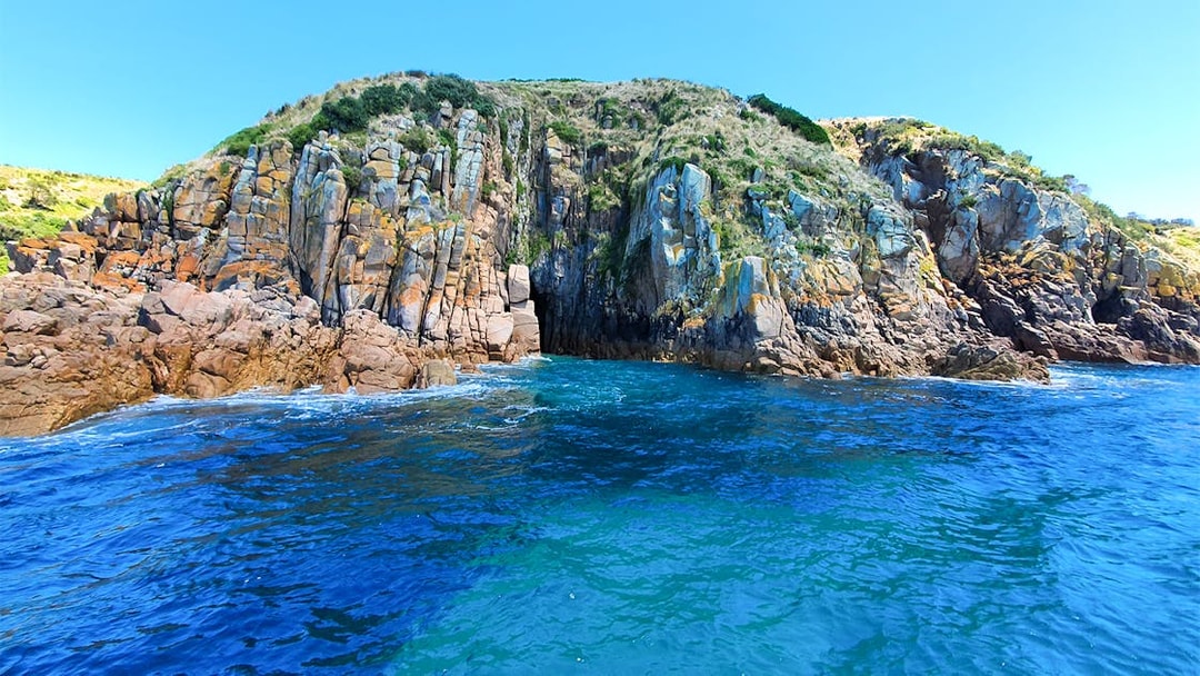 Cruise boat near rugged coastal cliffs at Cape Woolamai, Phillip Island.