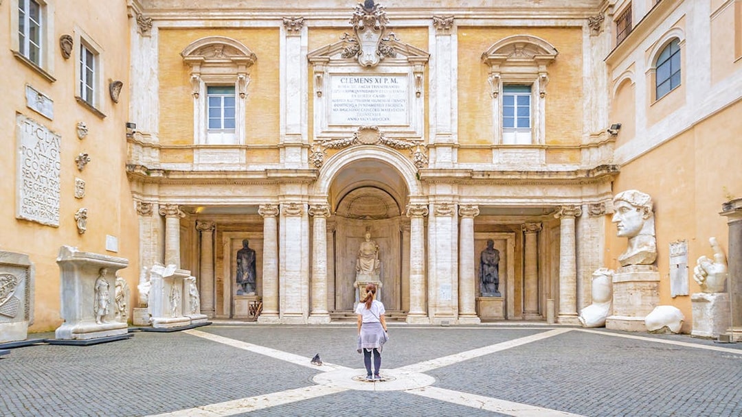 Girl standing in courtyard of Capitoline Museum, Rome, surrounded by ancient sculptures.