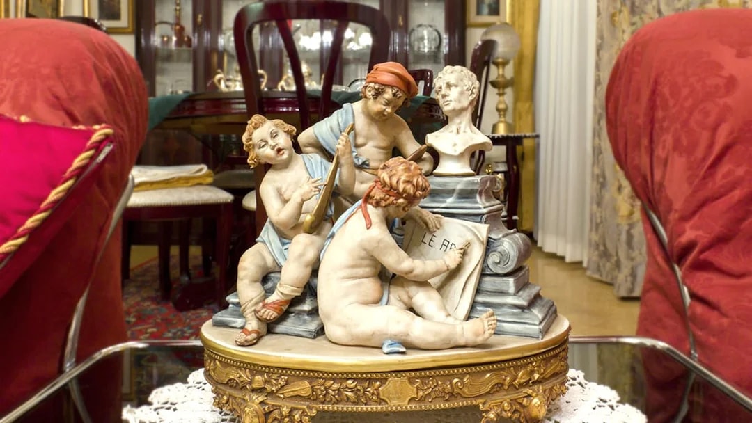 Capodimonte porcelain figurines depicting cherubs with musical instruments and a bust in an ornate room.