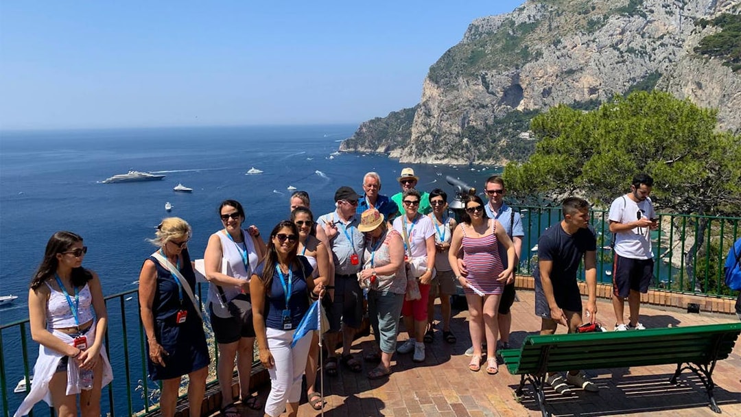 Tour group enjoying a scenic view of Capri Island cliffs and sea during a guided tour with boat ride.